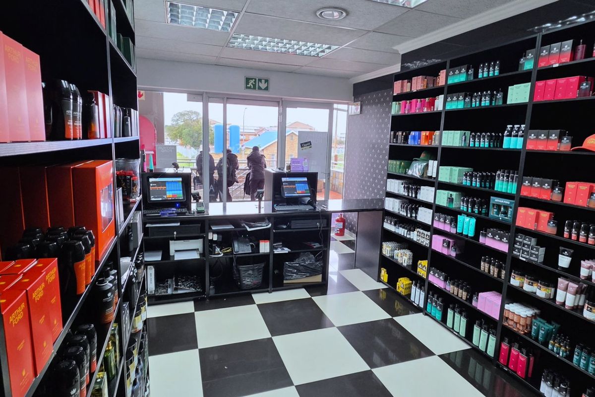 A commercial retail space featuring built-in black shelving units, a central check-out counter, and a distinctive black and white checkered floor.