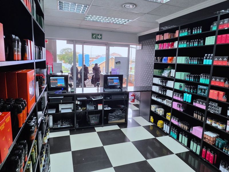 A commercial retail space featuring built-in black shelving units, a central check-out counter, and a distinctive black and white checkered floor.