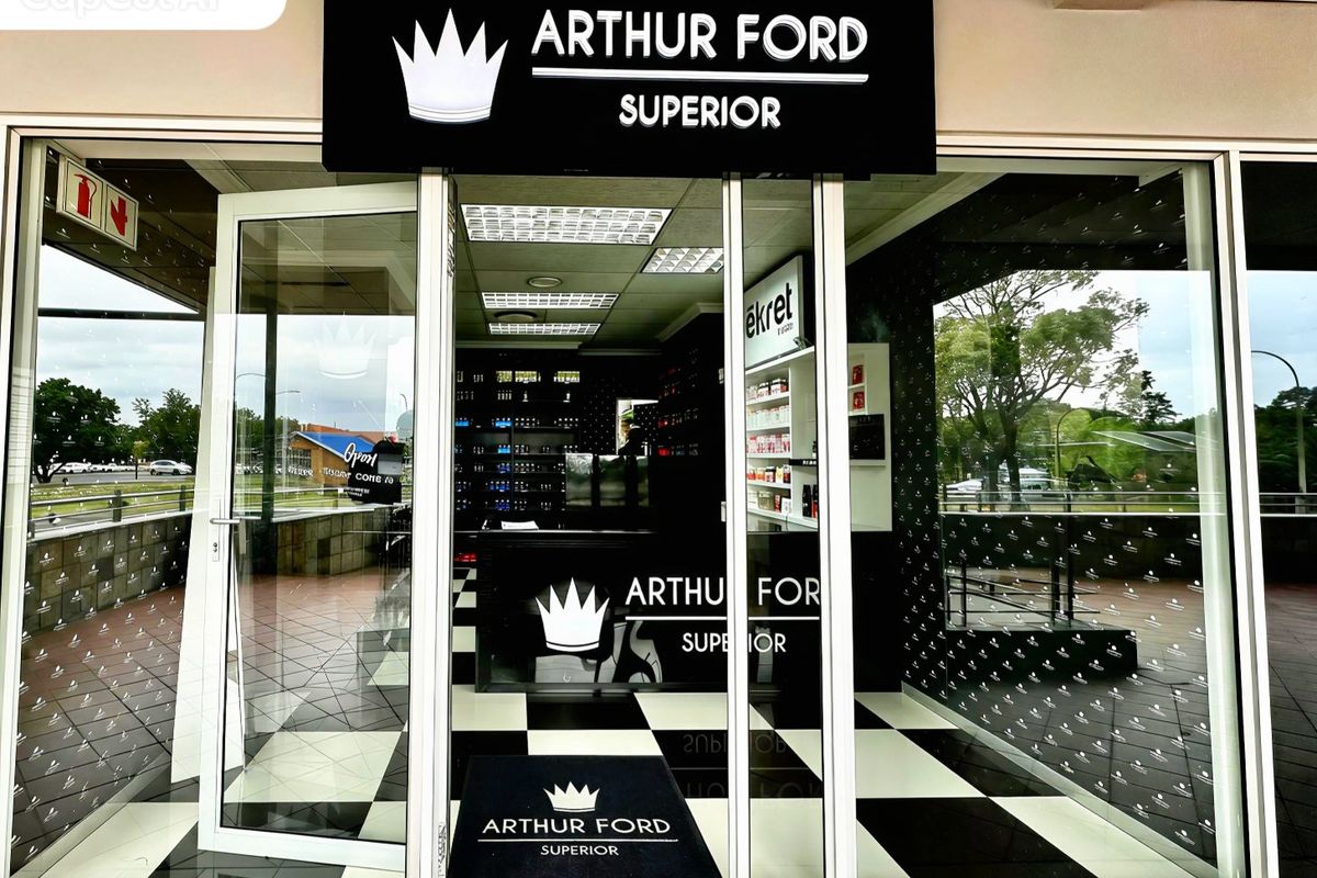 A commercial storefront entrance featuring a glass facade, branded signage, and a modern interior with checkered flooring and built-in display shelving.