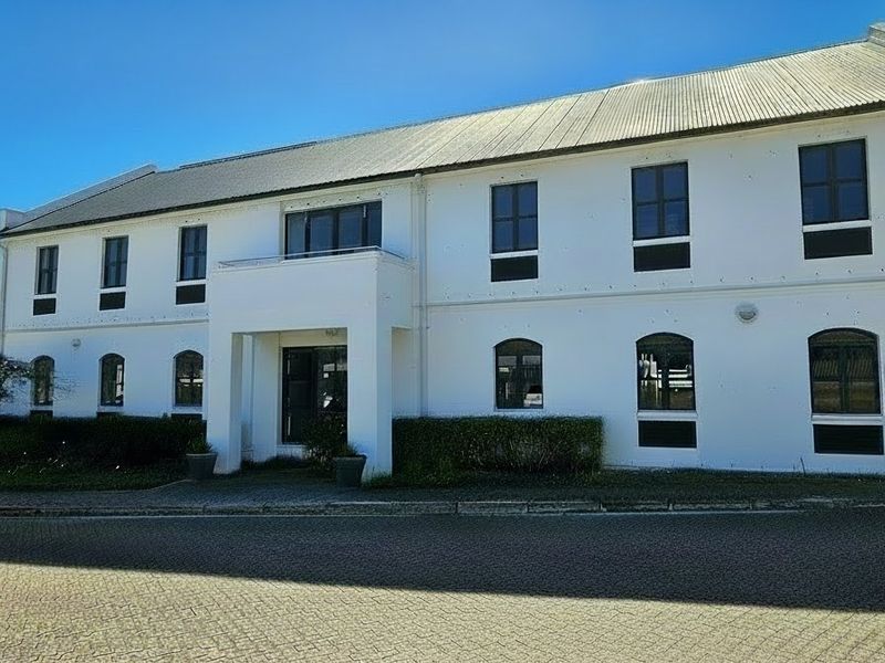 A well-maintained commercial office building featuring a white facade, corrugated metal roof, and paved driveway access.