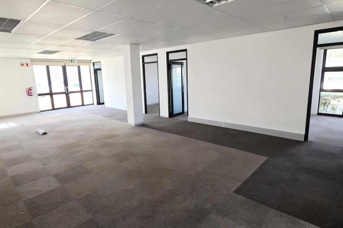 Spacious open-plan commercial office area featuring carpet tiles, suspended ceilings, and large aluminium-framed windows providing ample natural light.