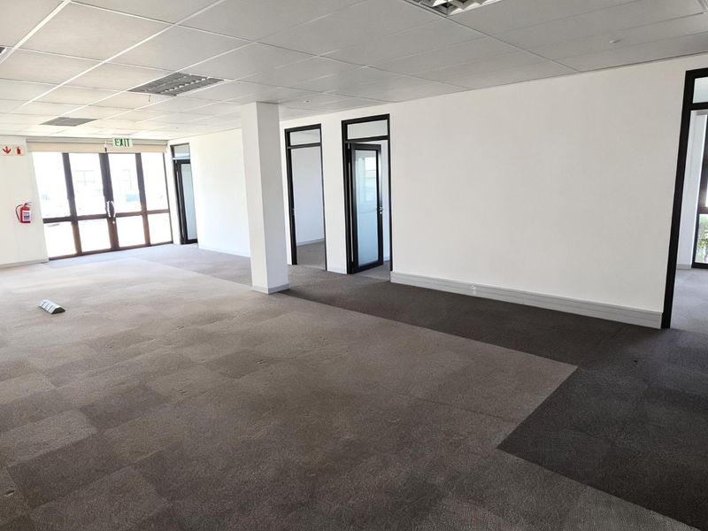 Spacious open-plan commercial office area featuring carpet tiles, suspended ceilings, and large aluminium-framed windows providing ample natural light.