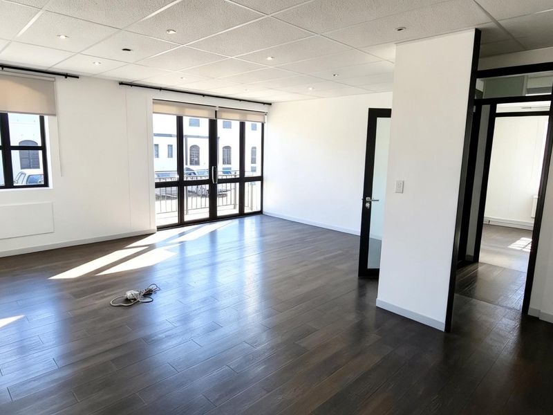 A bright, open-plan office space featuring modern laminate flooring, recessed ceiling lights, air conditioning, and large windows with roller blinds.