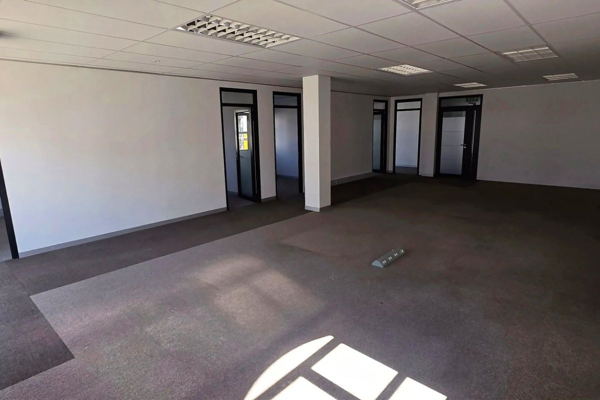 Spacious, open-plan commercial office area featuring suspended ceilings, recessed lighting, carpeted flooring, and wall-mounted air conditioning units.