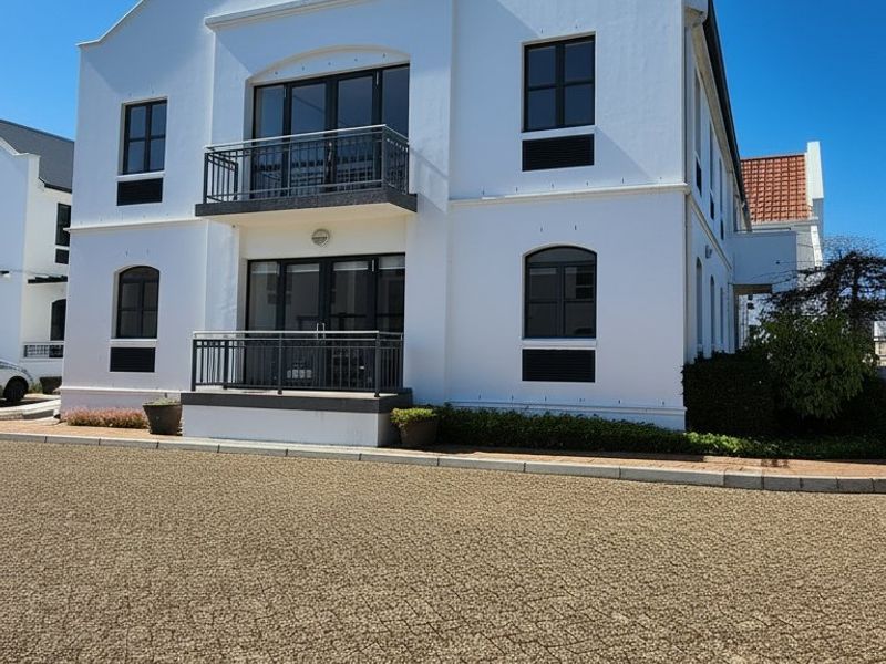 A well-maintained commercial building facade featuring white exterior walls, two levels of balconies with metal railings, and a paved driveway entrance.