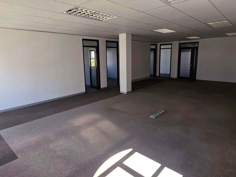 Spacious, open-plan commercial office area featuring suspended ceilings, recessed lighting, carpeted flooring, and wall-mounted air conditioning units.