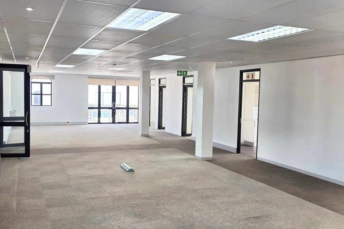 Spacious open-plan commercial office area featuring a suspended ceiling, recessed lighting, carpeted flooring, and essential fire safety equipment.