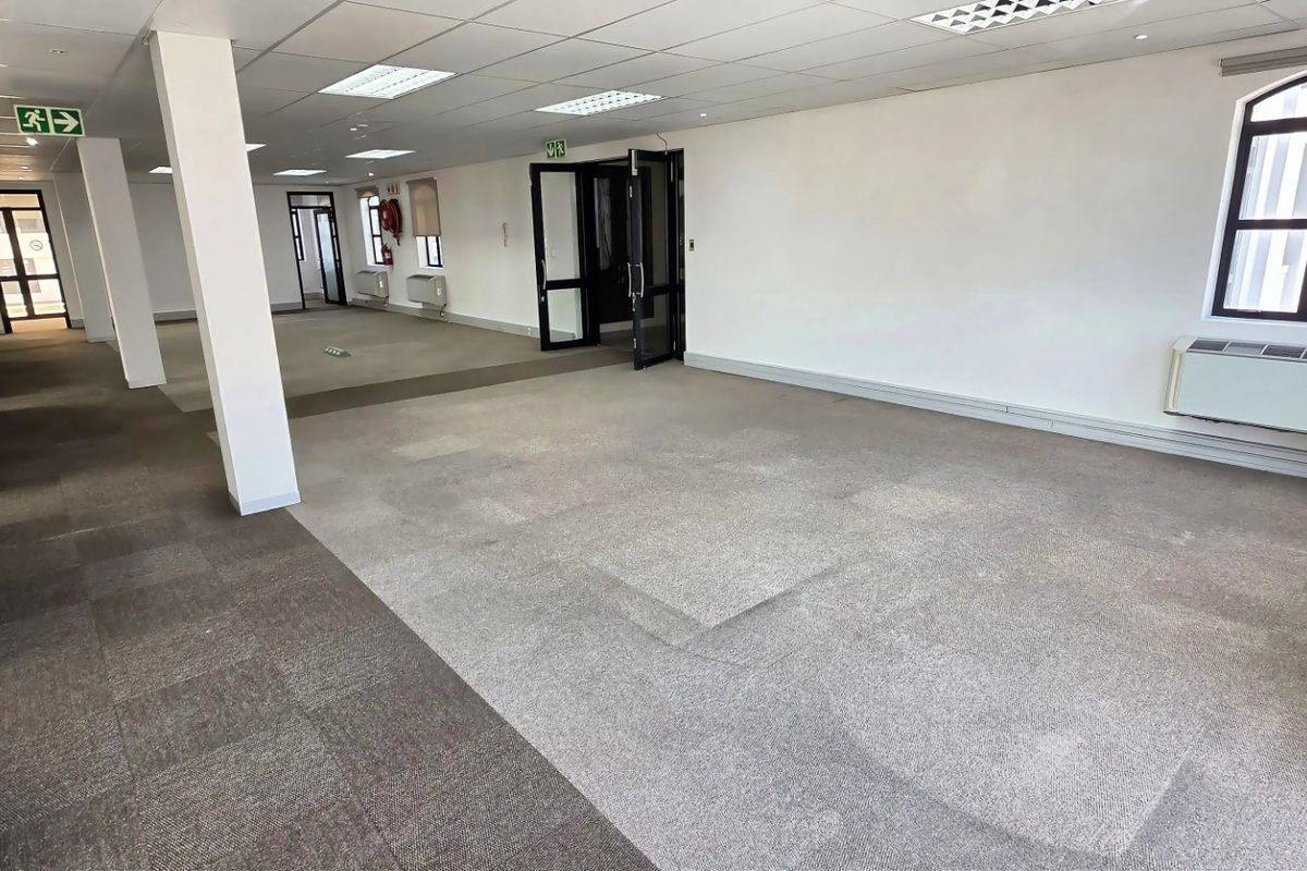 Spacious open-plan commercial office space featuring neutral carpeted flooring, suspended ceilings with recessed lighting, and integrated air conditioning units.