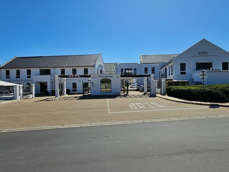 Front exterior view of a commercial office complex featuring a gated entrance, paved driveway, and well-maintained white building facades.