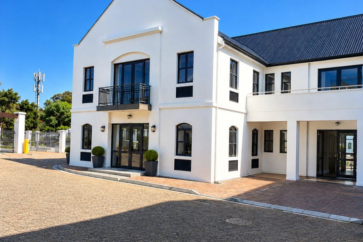 A well-maintained commercial building featuring a clean white facade, black framed windows, a metal roof, and a spacious cobblestone driveway.