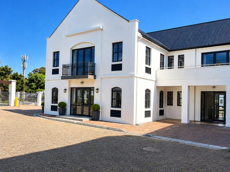 A well-maintained commercial building featuring a clean white facade, black framed windows, a metal roof, and a spacious cobblestone driveway.