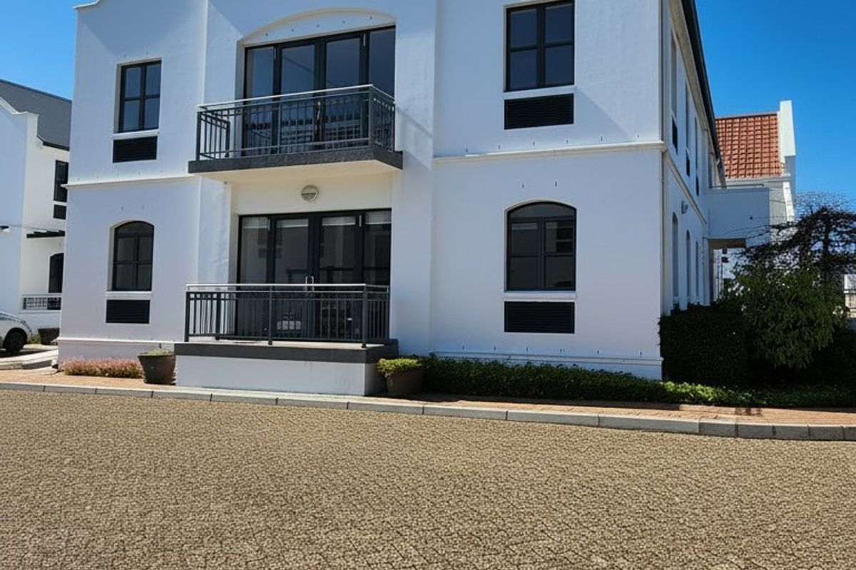 A well-maintained commercial building facade featuring white exterior walls, two levels of balconies with metal railings, and a paved driveway entrance.