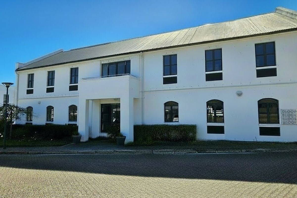 A well-maintained commercial office building featuring a white facade, corrugated metal roof, and paved driveway access.