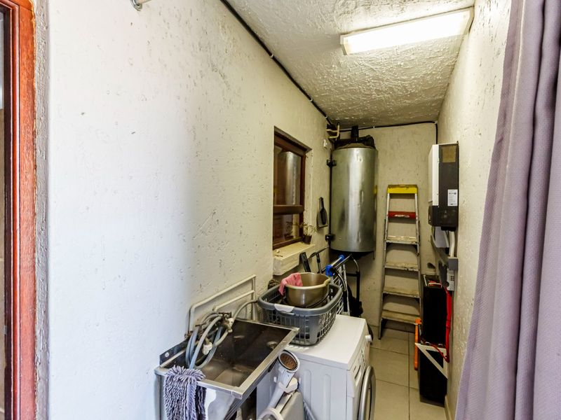 A functional laundry utility space featuring a geyser, stainless steel sink, and tiled flooring, requiring some cosmetic maintenance to the wall finishes.