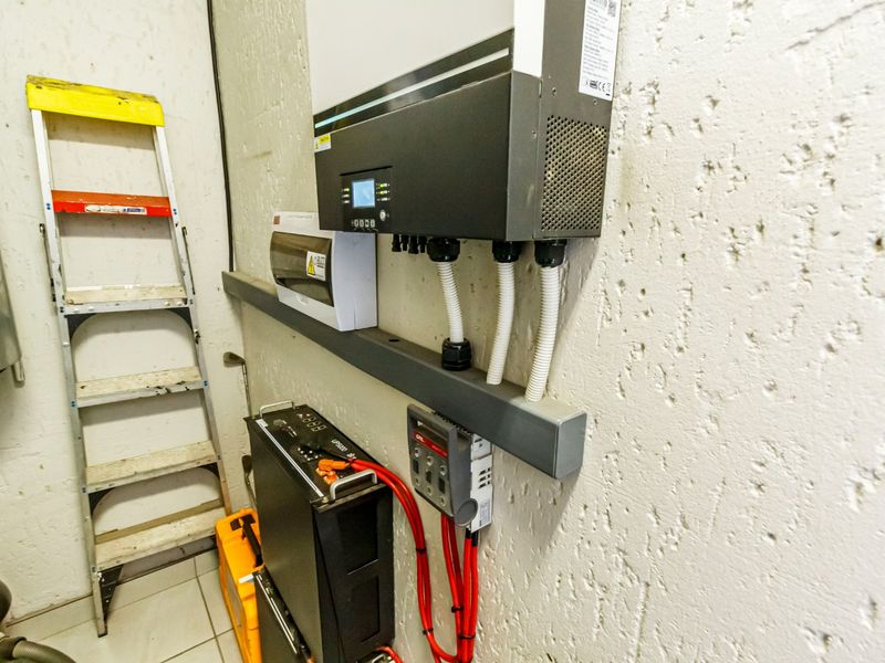 A utility space featuring a wall-mounted solar inverter, battery storage system, and electrical distribution board with organized conduit wiring.
