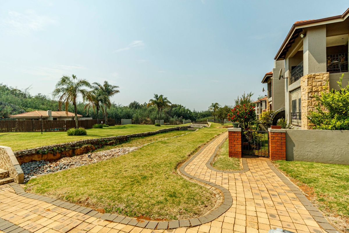 A view of the rear exterior featuring a paved walkway, landscaped garden, stone drainage channel, and a brick retaining wall leading to the townhouse.