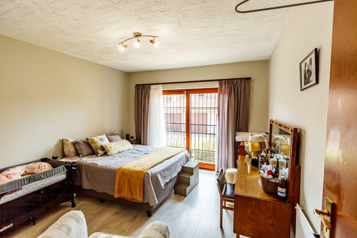 A well-lit bedroom featuring laminate flooring and a sliding glass door with a security gate, providing access to an outdoor area.