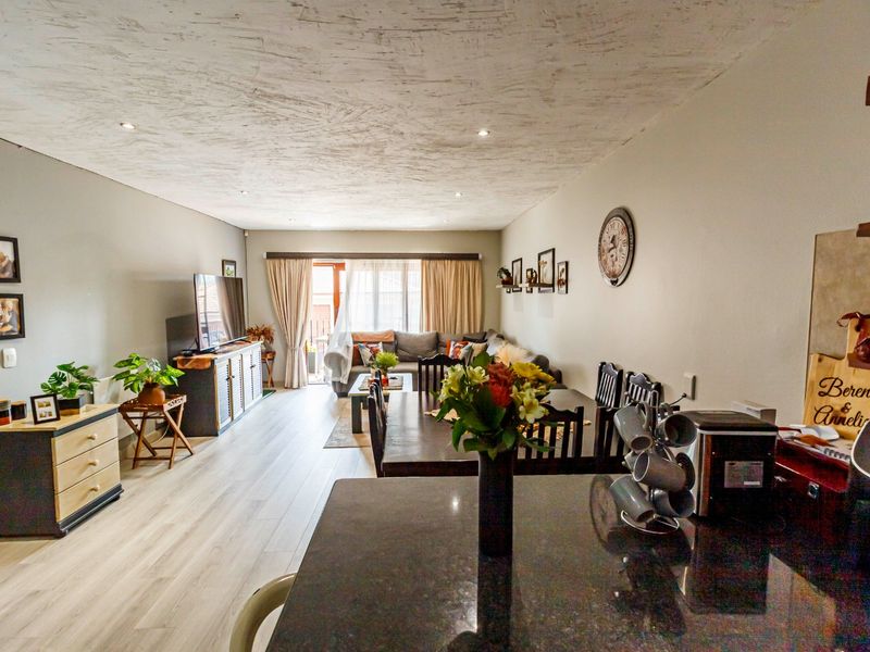 Spacious open-plan living and dining area featuring modern laminate flooring, recessed lighting, and a sleek granite kitchen countertop, leading to a patio.