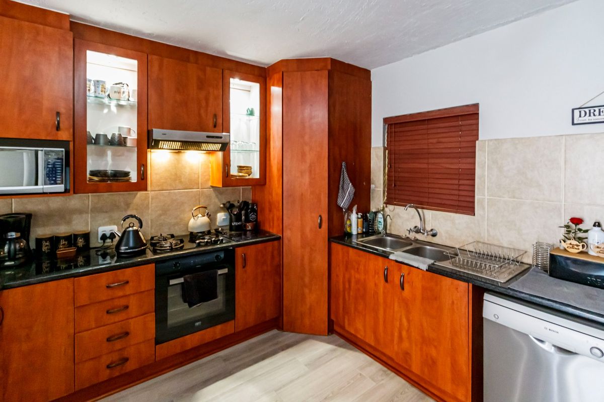 A functional kitchen featuring warm-toned wooden cabinetry, granite countertops, a built-in oven with gas hob, and a double basin sink with tiled backsplash.