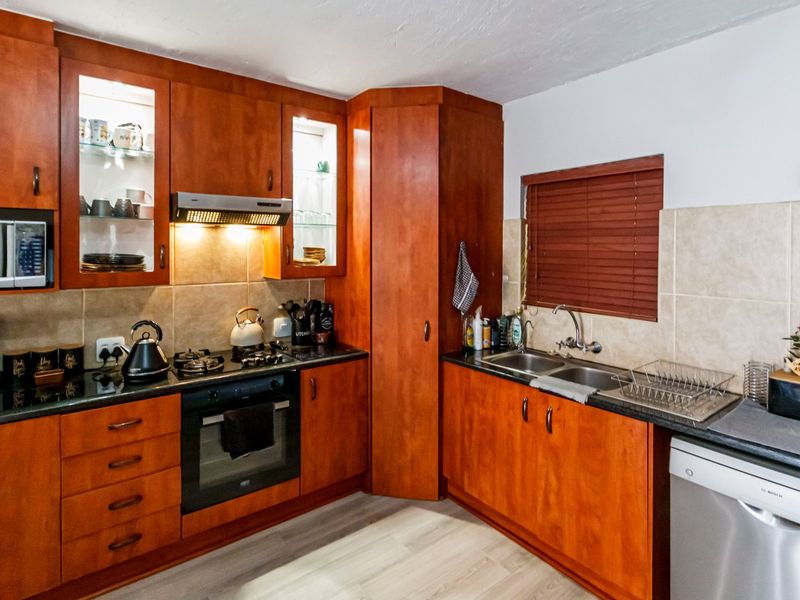 A functional kitchen featuring warm-toned wooden cabinetry, granite countertops, a built-in oven with gas hob, and a double basin sink with tiled backsplash.