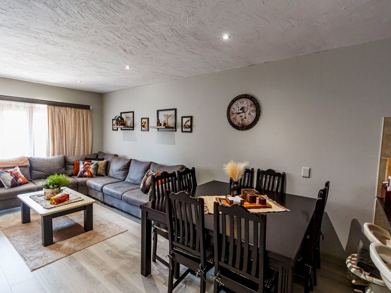 An open-plan living and dining area featuring modern laminate flooring, recessed ceiling lighting, and neutral wall finishes, creating a comfortable and cohesive living space.