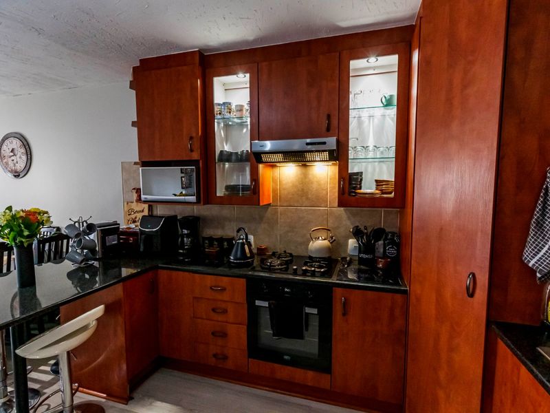 A functional kitchen featuring warm-toned wooden cabinetry, granite countertops, a gas hob, built-in oven, and an integrated breakfast bar for casual dining.