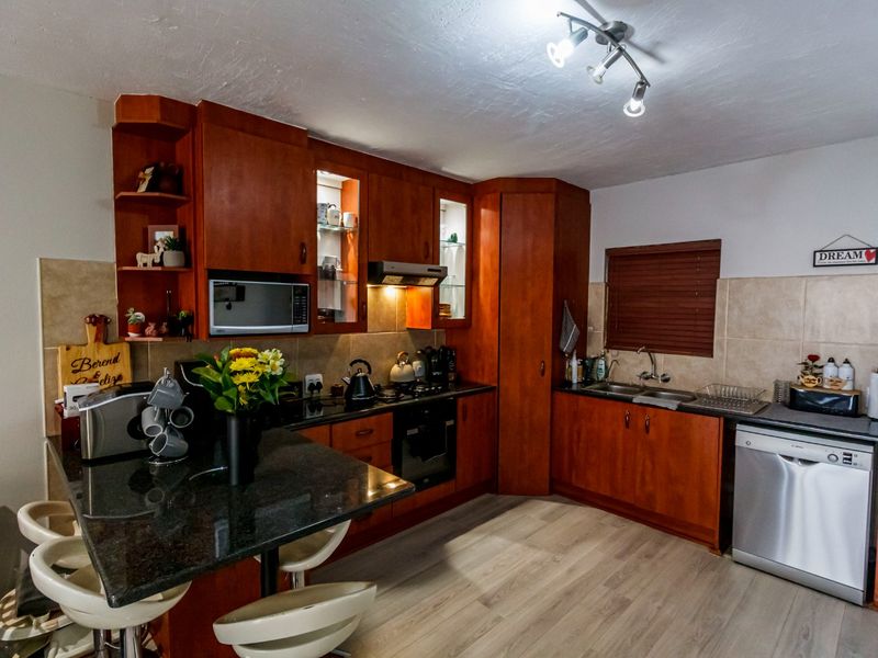 A well-maintained kitchen featuring warm-toned wooden cabinetry, granite countertops, a built-in oven, gas hob, and a functional double sink layout.