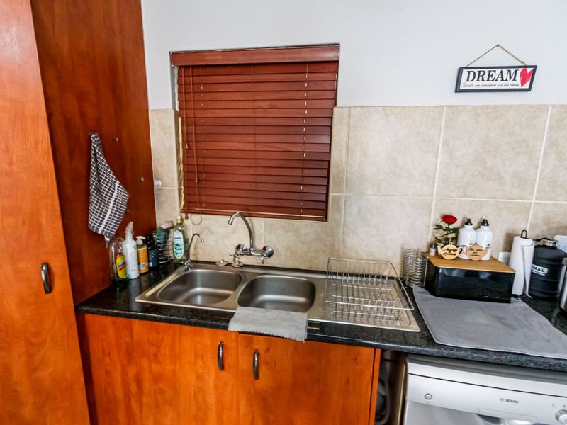 A functional kitchen area featuring wooden cabinetry, a double bowl stainless steel sink, tiled backsplash, and a window with wooden venetian blinds.