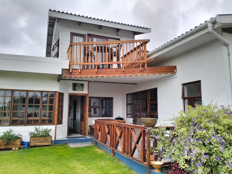 Rear view of the property featuring a wooden balcony, ground-level timber deck, and white exterior walls with timber-framed windows and doors.