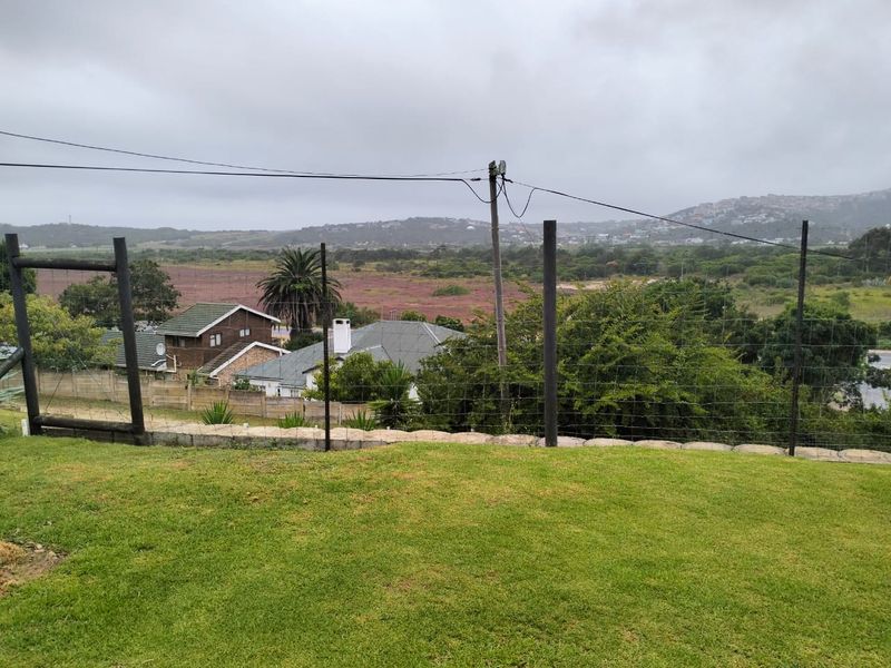 An elevated view overlooking a landscaped lawn, wire fencing, and surrounding residential neighborhood under an overcast sky.