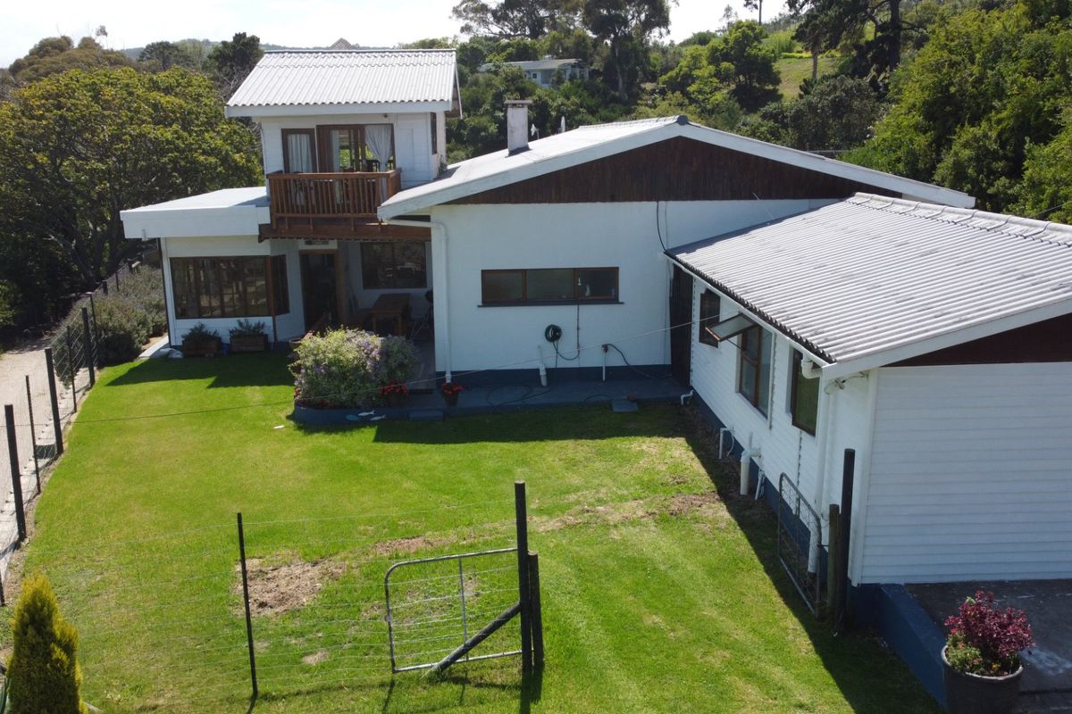 An elevated view of the rear of the property, featuring a multi-level structure with a corrugated metal roof, timber balcony, and a spacious lawn area.