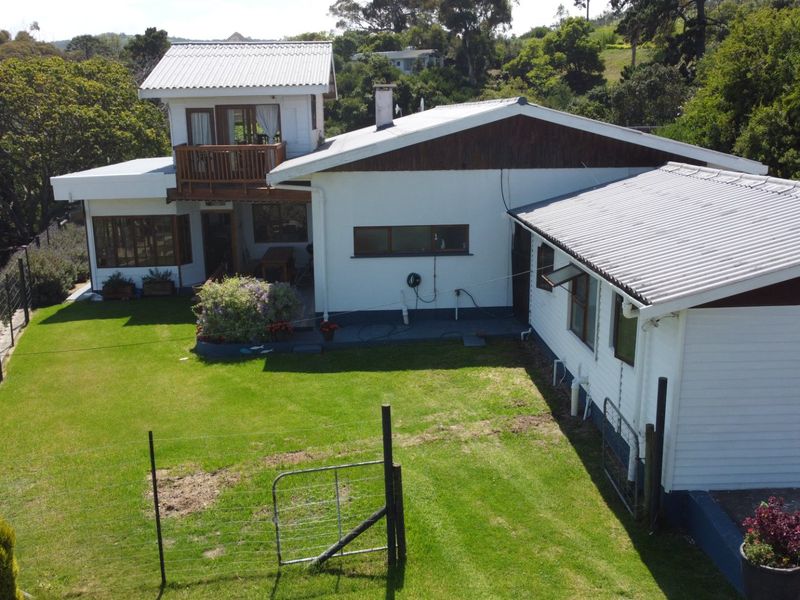 An elevated view of the rear of the property, featuring a multi-level structure with a corrugated metal roof, timber balcony, and a spacious lawn area.