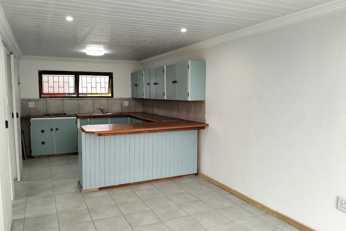 A functional, empty kitchen featuring light blue cabinetry, a breakfast bar, tiled flooring, and a neutral tiled backsplash.