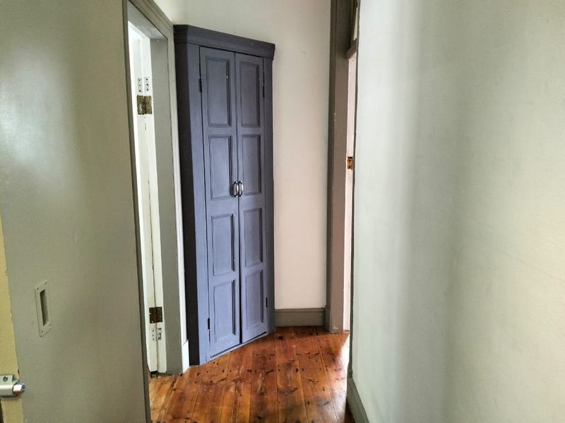 A narrow hallway featuring original timber flooring and a built-in corner storage cupboard with panelled doors.
