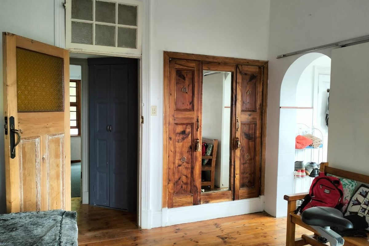 Bedroom featuring original timber flooring, built-in wooden wardrobe with central mirror, and an arched doorway leading to an adjacent space.