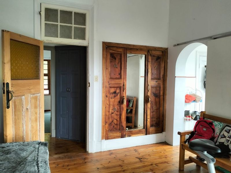 Bedroom featuring original timber flooring, built-in wooden wardrobe with central mirror, and an arched doorway leading to an adjacent space.