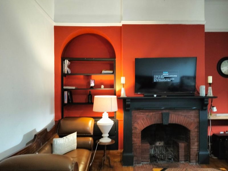 A living room featuring a prominent brick fireplace with a mantelpiece and a built-in arched shelving unit set against a bold red feature wall.