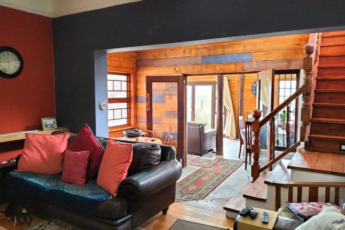 A living room featuring timber wall paneling, wooden flooring, and a wooden staircase leading to an upper level, with access to an adjacent room.