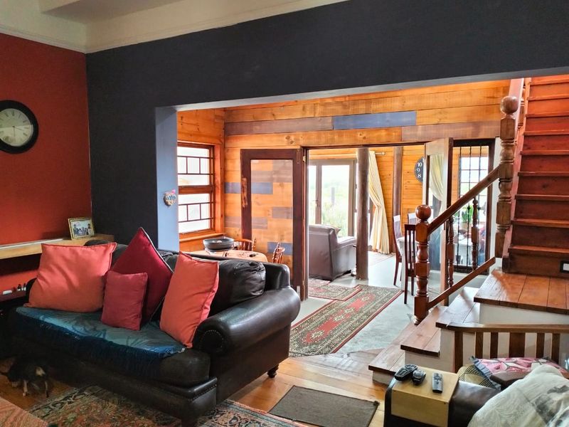 A living room featuring timber wall paneling, wooden flooring, and a wooden staircase leading to an upper level, with access to an adjacent room.