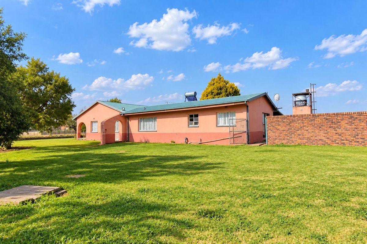 Rear view of the farmhouse featuring a metal roof, solar water heating system, water storage tank, and a spacious surrounding lawn.