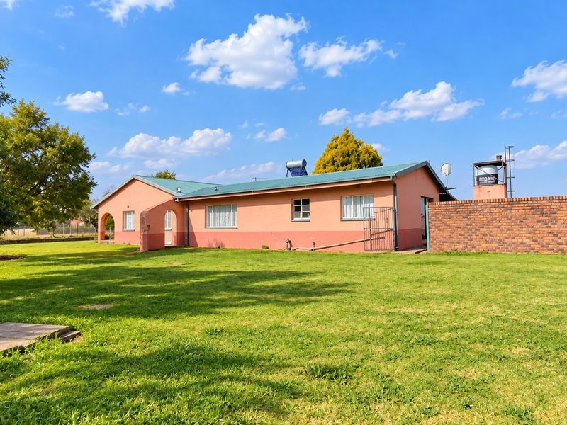 Rear view of the farmhouse featuring a metal roof, solar water heating system, water storage tank, and a spacious surrounding lawn.