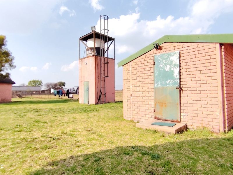 Exterior view of a farm property featuring a brick outbuilding and a water tower structure set within a grassy yard.
