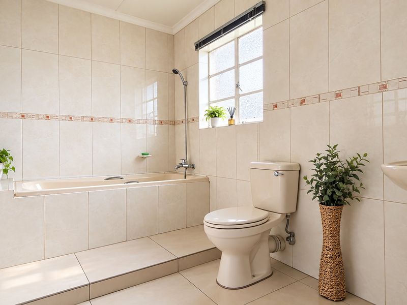 A well-maintained bathroom featuring a built-in bathtub, pedestal basin, toilet, and neutral floor-to-ceiling wall tiles.