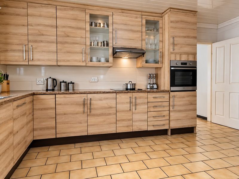 A well-maintained kitchen featuring light wood-grain cabinetry, granite countertops, built-in oven, extractor fan, and durable ceramic tile flooring.