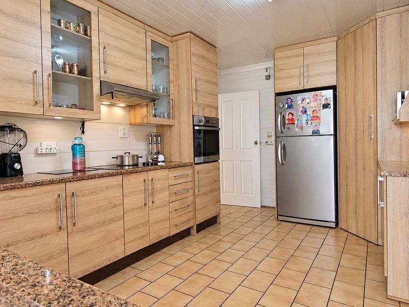 A functional kitchen featuring light wood-grain cabinetry, granite countertops, built-in oven, extractor fan, and durable ceramic tile flooring.