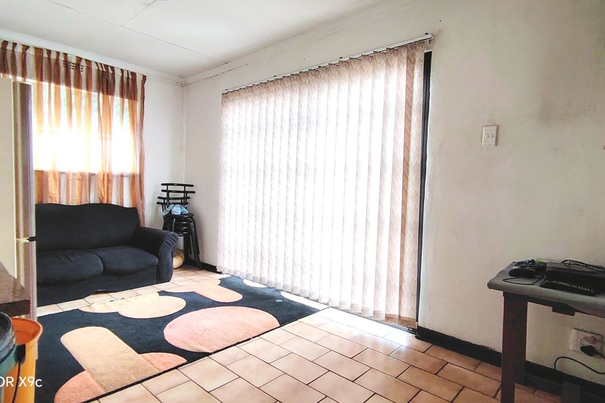 A living room area featuring tiled flooring and vertical blinds, requiring some cosmetic updates to the wall finishes.