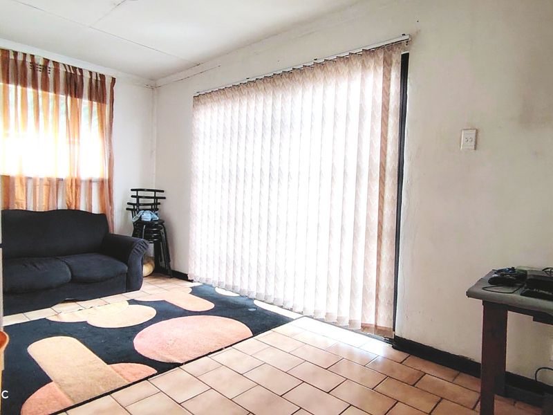 A living room area featuring tiled flooring and vertical blinds, requiring some cosmetic updates to the wall finishes.