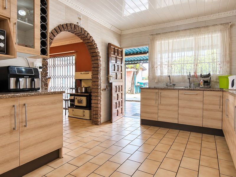 A functional kitchen featuring light wood cabinetry, granite countertops, tiled flooring, and a distinctive brick archway leading to an adjacent living area.