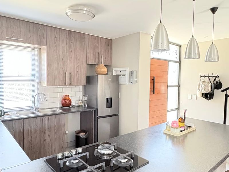 Modern kitchen featuring wood-grain cabinetry, stone countertops, a gas hob, and a subway tile backsplash, seamlessly integrated into an open-plan living space.