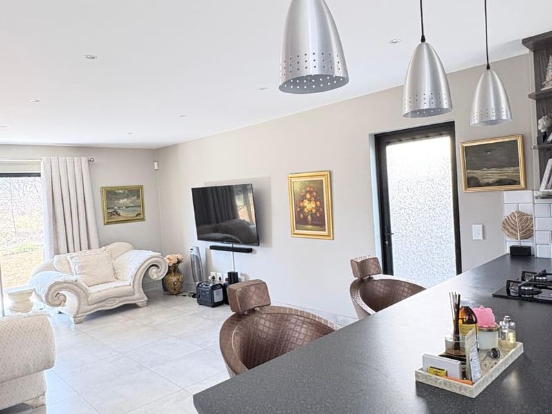 Spacious open-plan living area featuring a modern kitchen island with a built-in hob, tiled flooring, and recessed lighting, seamlessly connecting to the lounge space.